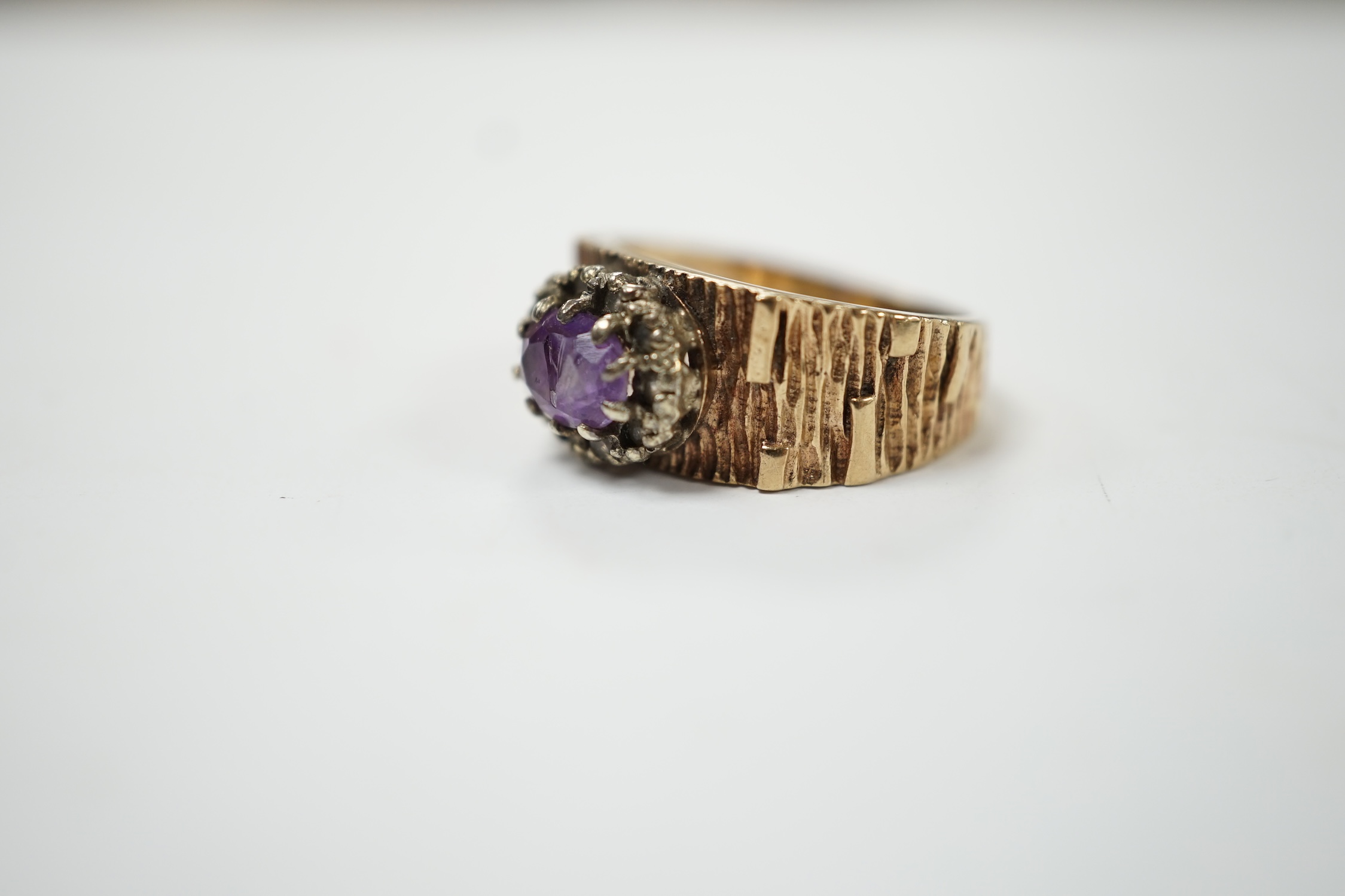 A textured yellow metal, amethyst and simulated diamond set oval cluster ring, size M, gross weight 4.4 grams. Fair condition